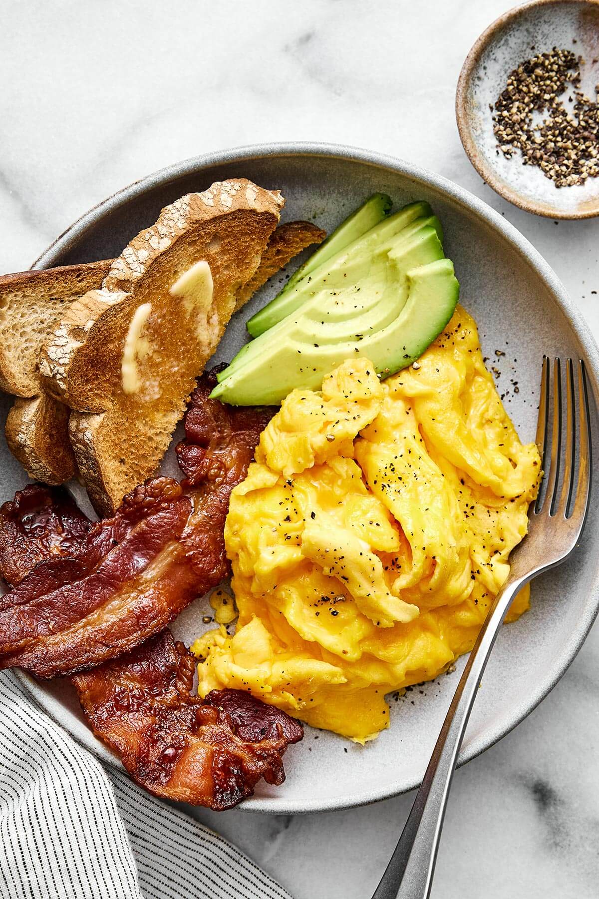 Learn how to make scrambled eggs with my easy, foolproof method! Your eggs will turn out silky and creamy every single time. Scrambled eggs with bacon, avocado, and toast.