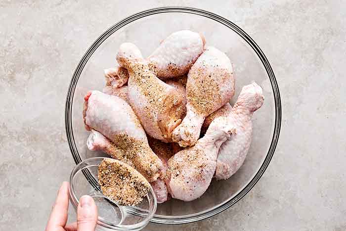 Pouring dry rub on chicken drumsticks.
