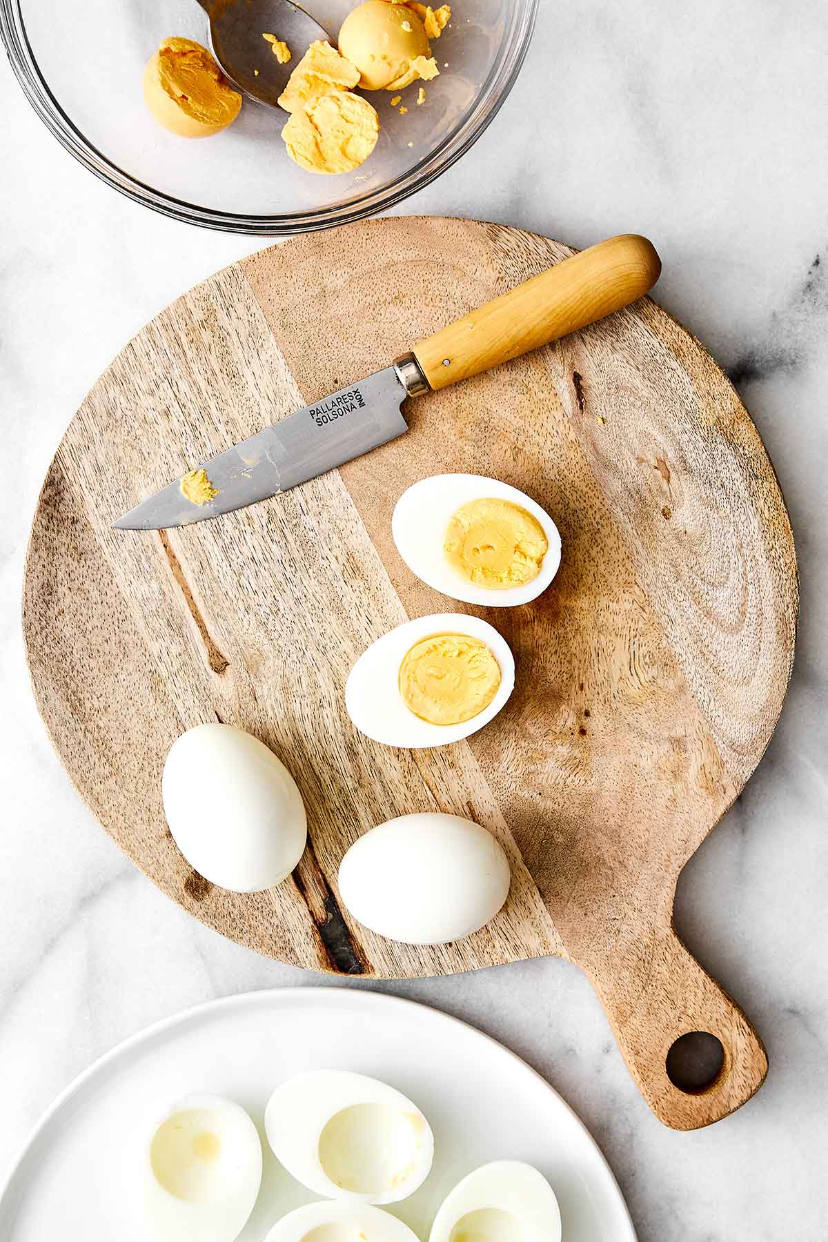Slicing deviled eggs in half on a cutting board.