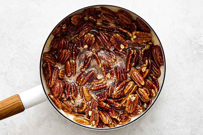 Boiling pecans and maple syrup in a pot.