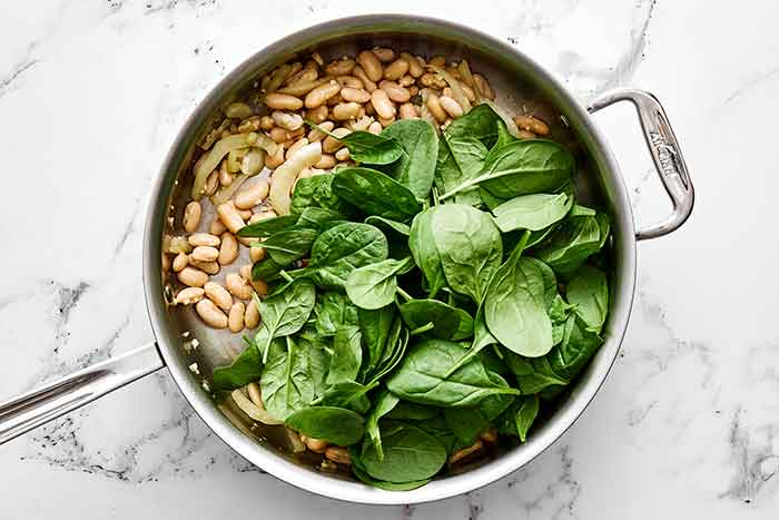 Step three of spinach and white bean salad: add the spinach.