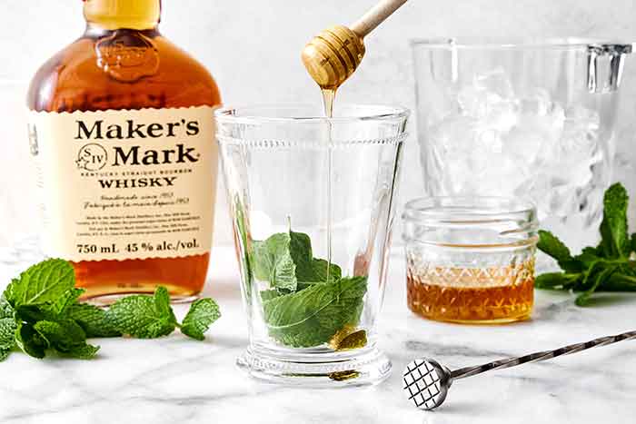 Adding sweetener to a mint julep cocktail.