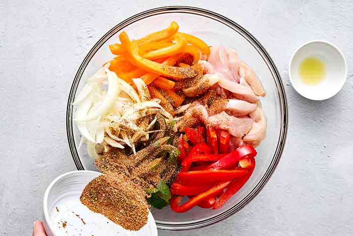 Step two of sheet pan chicken fajitas: toss everything with seasoning.
