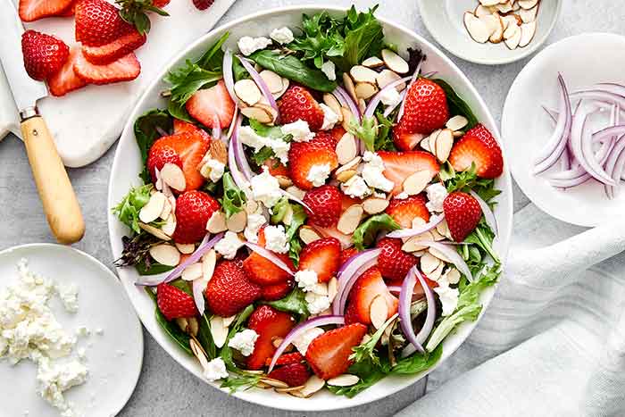 Assembling a strawberry salad in a bowl.