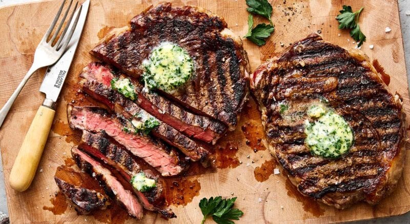 Sliced grilled ribeye steaks on a wooden board.
