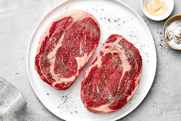 Seasoning ribeye steaks on a plate.