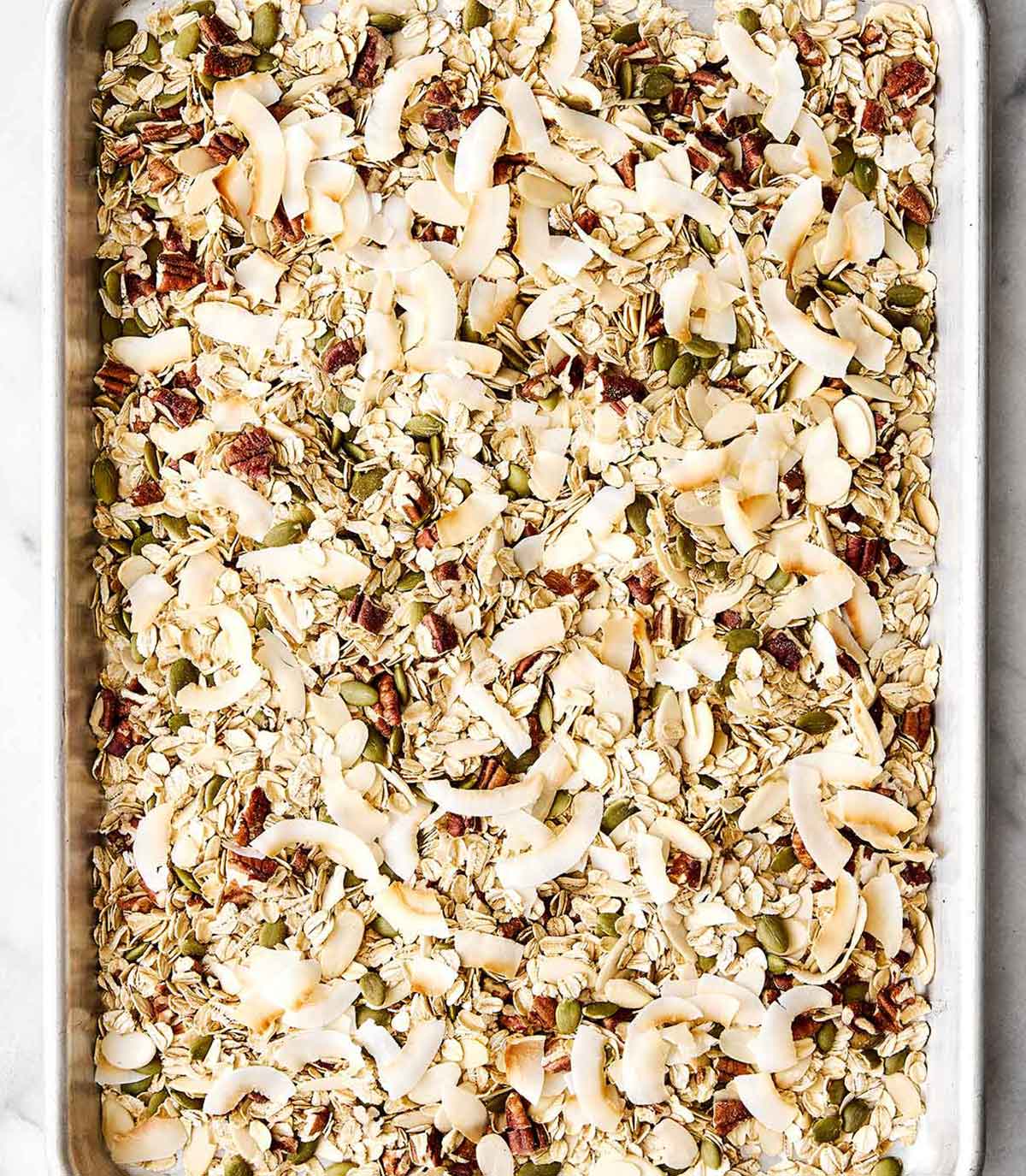 Toasting coconut flakes with muesli ingredients on a sheet pan.