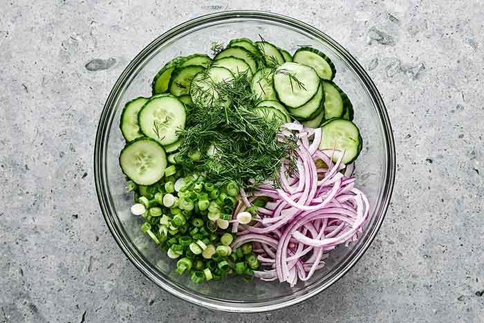 Adding creamy cucumber salad ingredients to a bowl.