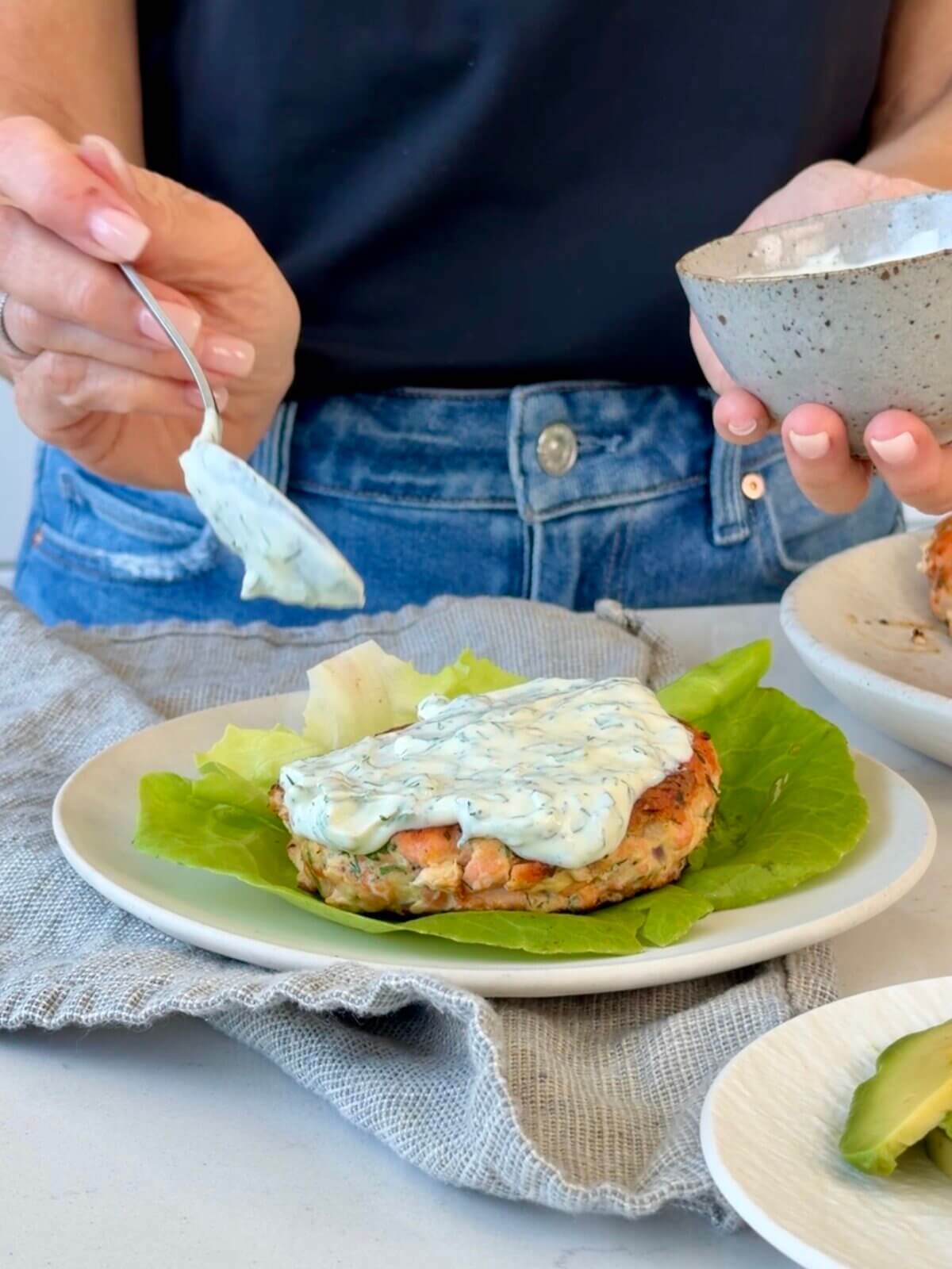 Dolloping the lemon dill yogurt sauce on a salmon burger.