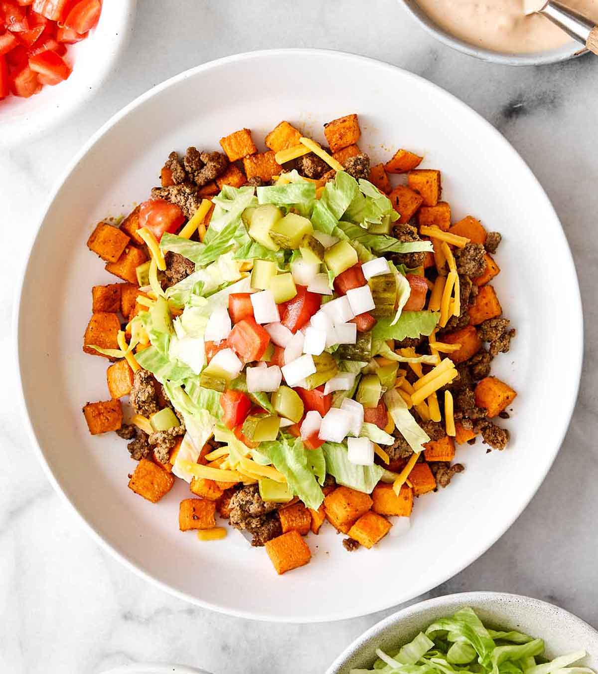 This sweet potato burger bowl is the best kind of weeknight dinner. It's all the tasty layers of an In-N-Out burger, but leans healthier! Piling ingredients for a sweet potato burger bowl.