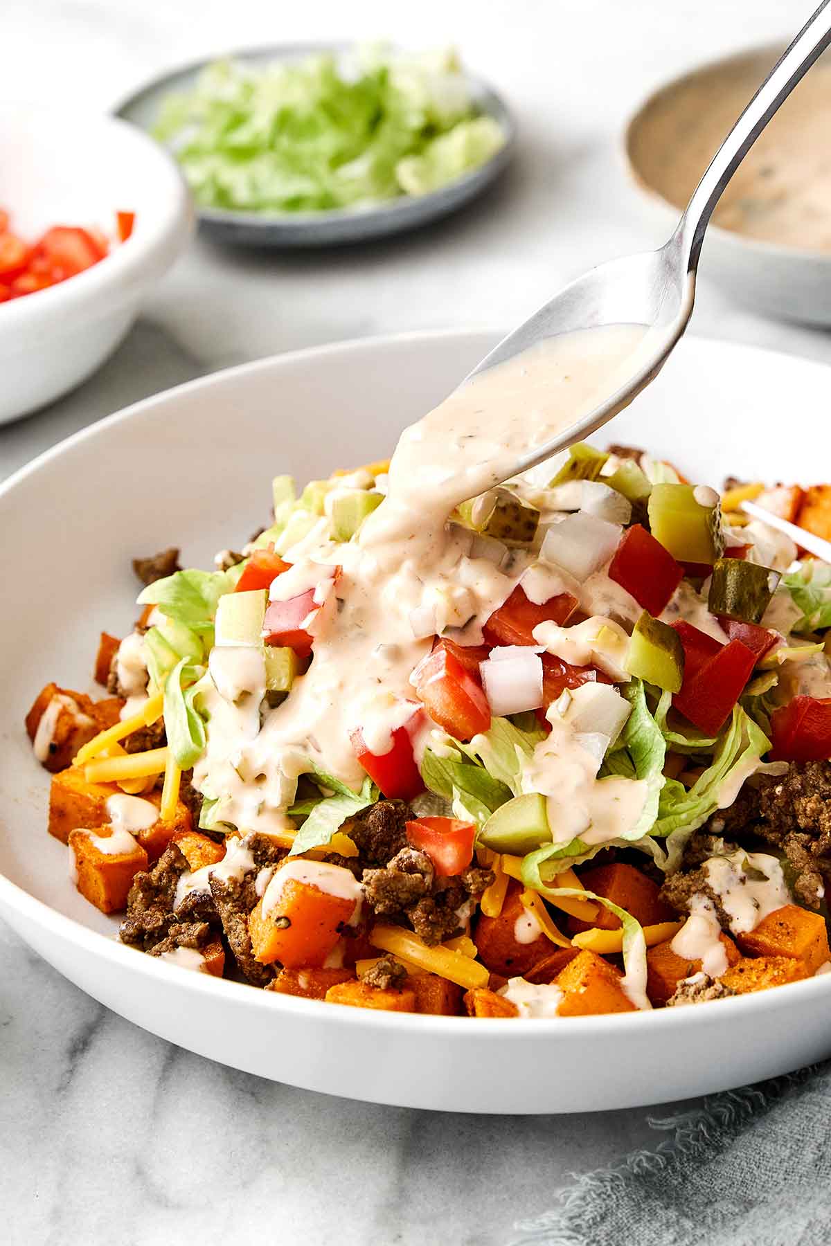This sweet potato burger bowl is the best kind of weeknight dinner. It's all the tasty layers of an In-N-Out burger, but leans healthier! Pouring In-N-Out sauce on a sweet potato burger bowl.
