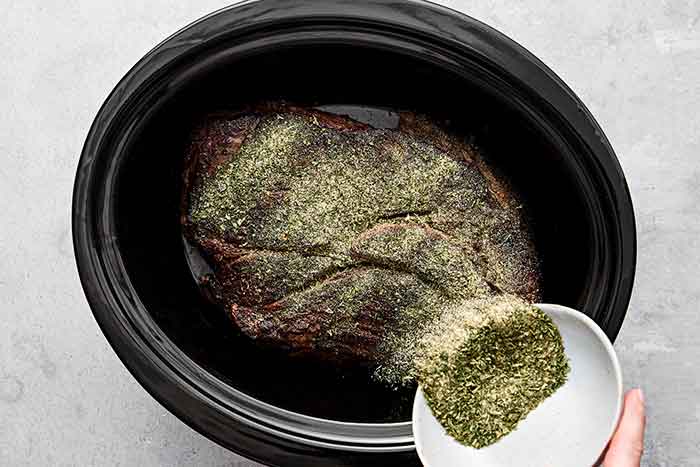 Adding seasoning to chuck roast in a crockpot.