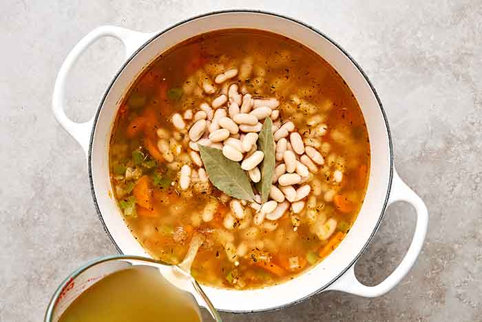 Adding broth and beans into a Tuscan soup.