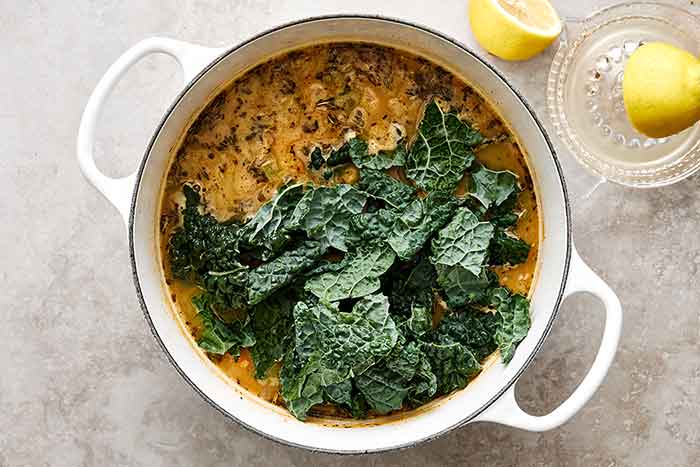 Adding kale into a white bean soup.