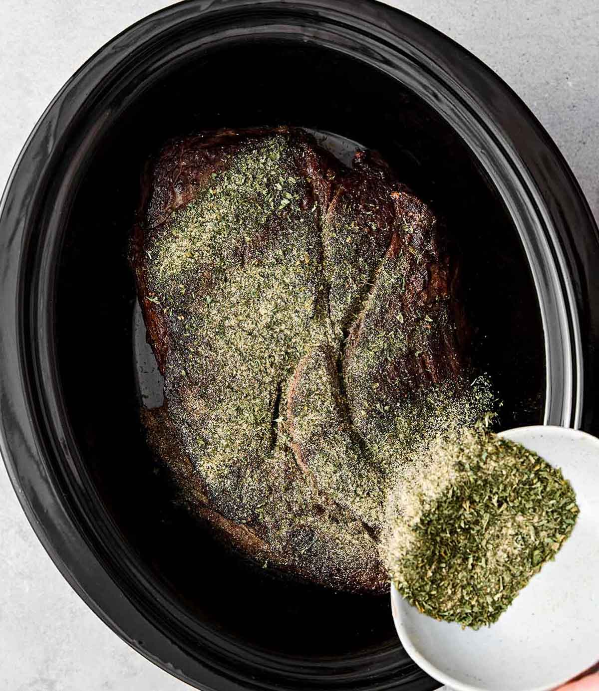 Adding seasoning to chuck roast in a crockpot.