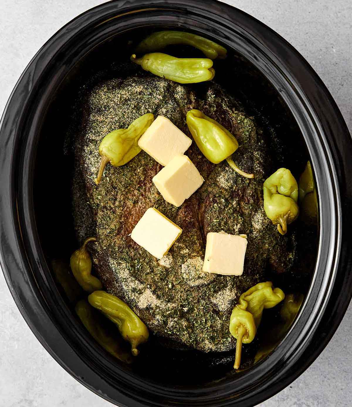 Adding butter and banana peppers to chuck roast in a crockpot.
