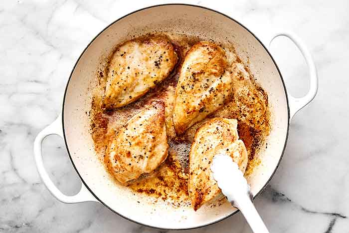 Searing chicken breasts in a pan.