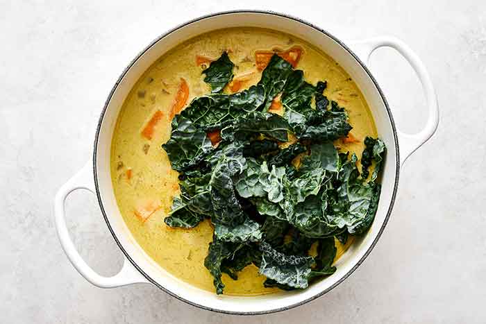 Adding kale to a sweet potato stew.